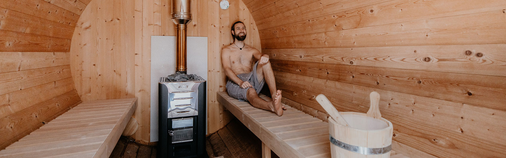 Fasslsauna von innen - junger Mann lehnt an der Wand der Sauna und genießt das Schwitzen.