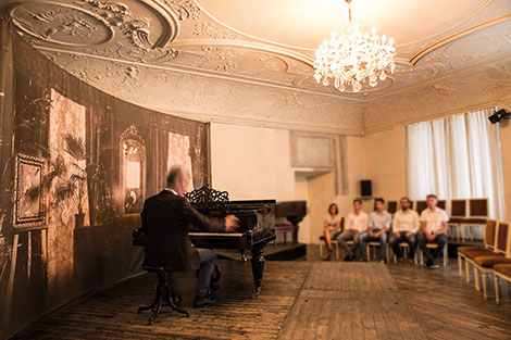 Mann spielt auf dem Klavier und die Zuhörer im Hintergrund lauschen den Klängen der Musik
